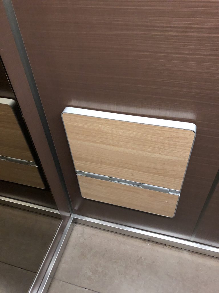 View of a folding seat attached to the wall of an elevator. The seat folded up.